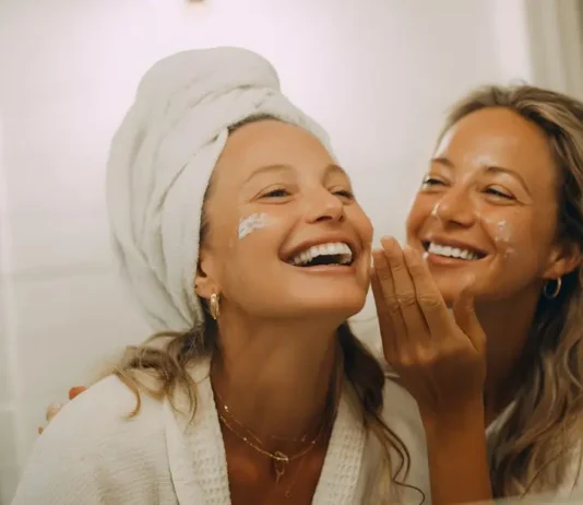 თავის მოვლა, როგორც ინვესტიცია საკუთარ თავში: თანამედროვე გზამკვლევი Two cheerful women applying face cream and enjoying a skincare routine together in a bathroom.