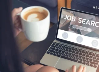 სტუდენტობიდან კარიერულ ჩიხამდე, როგორ იცვლება დასაქმების პარადიგმა საქართველოში A young person holding a coffee cup and searching for jobs on a laptop with "Job Search" on the screen.