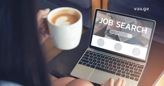 A young person holding a coffee cup and searching for jobs on a laptop with "Job Search" on the screen.