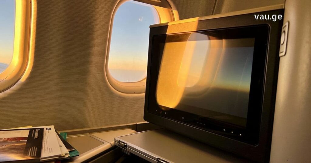 Airplane interior with a seat-back entertainment screen and sunset view through the windows.