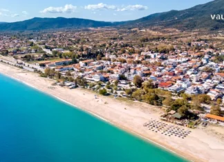 ჰალკიდიკი: საბერძნეთის ზურმუხტისფერი საგანძური Aerial view of a wide sandy beach and turquoise sea in Halkidiki, Greece, with coastal town and mountains.