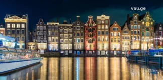 ამსტერდამი: ევროპული ვოიაჟი არხებისა და თავისუფლების სამყაროში Illuminated historic canal houses in Amsterdam at night with golden reflections on the water and a glass-top tour boat.