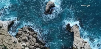 აია ნაპა: ხმელთაშუა ზღვის მარგალიტი – თქვენი დაუვიწყარი საზაფხულო თავგადასავალი Top-down aerial view of a rugged, light-tan coastline with sea stacks and crashing turquoise waves.