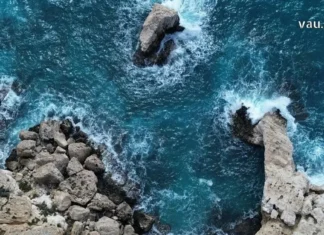 აია ნაპა: ხმელთაშუა ზღვის მარგალიტი – თქვენი დაუვიწყარი საზაფხულო თავგადასავალი Top-down aerial view of a rugged, light-tan coastline with sea stacks and crashing turquoise waves.