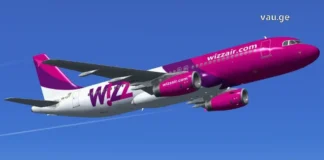 ვიმოგზაუროთ ჭკვიანურად – Wizz Air Georgia A side profile view of a Wizz Air Airbus A320 aircraft with its white, purple, and magenta livery, parked on the airport tarmac under a clear blue sky.